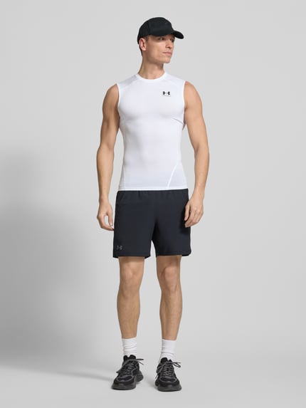 Männermodel trägt Slim Fit Top mit Logo-Print von Under Armour aus Elastischer-Material-Mix, Rundhalsausschnitt, schwarze Shorts, Ganzkörperansicht von vorne. Rückenlänge Größe M: 65 cm.
