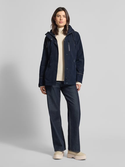 Modelka kobieca nosi Funktionsjacke mit Brusttasche od Gil Bret, dopasowany krój, kaptur, stójka, tunel, kieszeń na piersi na zamek, długość pleców w rozmiarze 36: 74 cm, szerokość ramion w rozmiarze 36: 41 cm, szerokość w biuście w rozmiarze 36: 47 cm, długość rękawa w rozmiarze 36: 65 cm, granatowy, gładka faktura, całkowity widok z przodu.