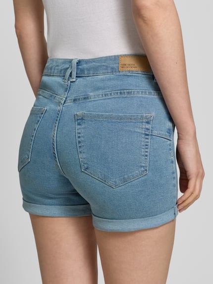 Frauenmodel trägt Regular Fit Jeansshorts aus Baumwoll-Mix Modell 'LUNA' von Vero Moda, Denim-Optik, Label-Patch, 5-Pocket-Design, Beinabschluss Umschlag, Nahaufnahme Rückansicht.