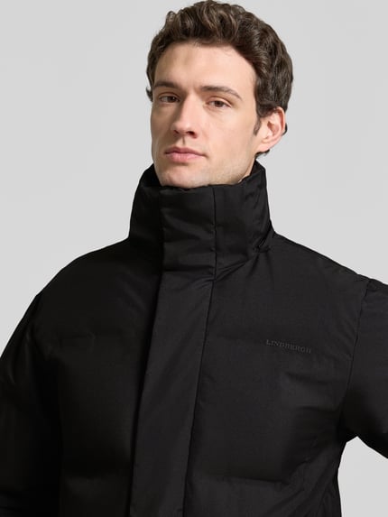 Männermodel trägt Regular Fit Steppmantel mit Eingrifftaschen von Lindbergh in Schwarz, glatte Struktur, Nahaufnahme Oberkörper.