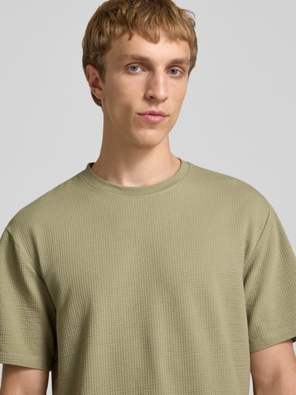 Männermodel trägt Regular Fit T-Shirt aus Baumwoll-Mix Modell 'KIAN' von Only & Sons in Optik: Unifarben mit Rundhals, Ärmelform: Kurzarm, Materialverarbeitung: Piqué, Nahaufnahme Oberkörper.