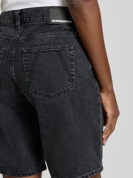 Frauenmodel trägt Regular Fit Jeansshorts aus reiner Baumwolle Modell 'THALINAA' von Armedangels in Denim-Optik mit Label-Patch, Twill-Material, Detailaufnahme Rückansicht.