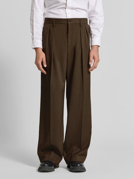 Männermodel trägt Relaxed Fit Stoffhose aus Baumwoll-Mix von Juvia in Braun mit Kellerfalten, Eingriff- und Gesäßtaschen, Ganzkörperansicht von vorne.