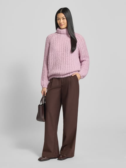 Modelka kobieca nosi Strickpullover mit Rollkragen od Smith and Soul w jasnoróżowym kolorze, luźny krój, dzianina z dodatkiem alpaki, żebrowane wykończenia, zdjęcie całej sylwetki od przodu.