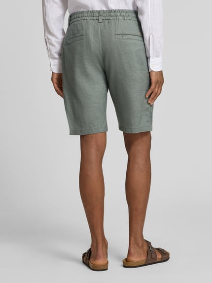 Männermodel trägt Tapered Chinoshorts aus Leinen-Mix Modell 'DS_3S' von BOSS Orange in Hellgrün, Leinenstruktur, Paspeltaschen, Ganzkörperansicht Rückansicht.