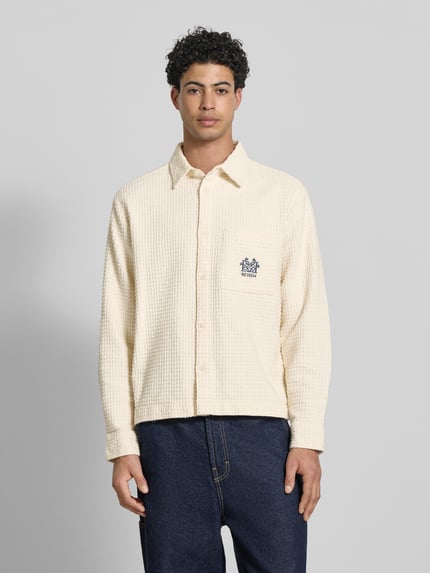 Männermodel trägt Regular Fit Freizeithemd mit Logo-Stitching von REVIEW aus cremefarbener Baumwolle mit Strukturmuster, Ganzkörperansicht von vorne.