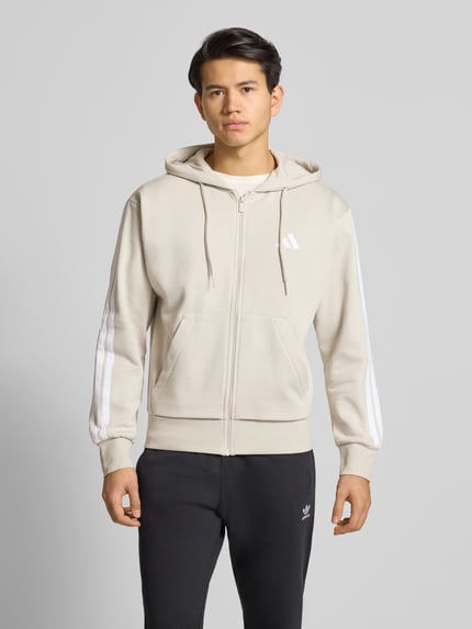 Männermodel trägt Regular Fit Sweatjacke mit Viskose-Anteil von adidas Sportswear im Baumwoll-Viskose-Mix, beige mit Logo-Stitching, Ganzkörperansicht von vorne.