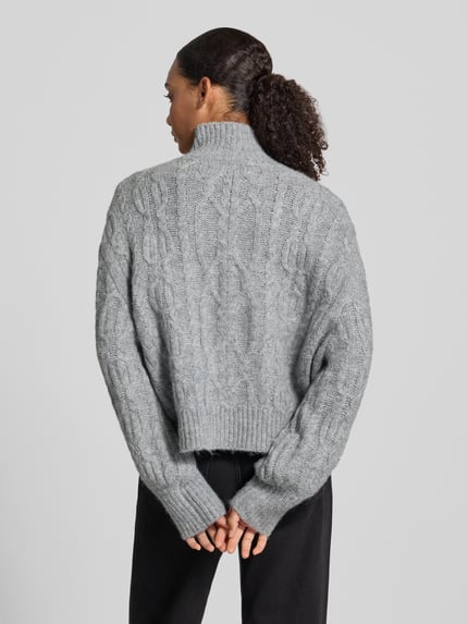 Frauenmodel trägt Pullover mit Zopfmuster Rumpfabschluss asymmetrisch von ONLY in Strickoptik, grau, Ganzkörperansicht Rückansicht.