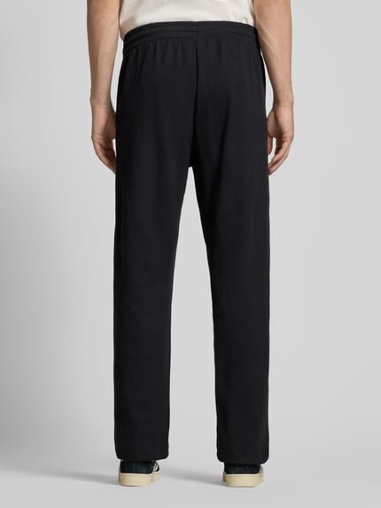 Männermodel trägt Straight Fit Sweatpants mit elastischem Bund Modell 'Essentials' von adidas Originals in Schwarz mit Strukturmuster, Ganzkörperansicht Rückansicht.