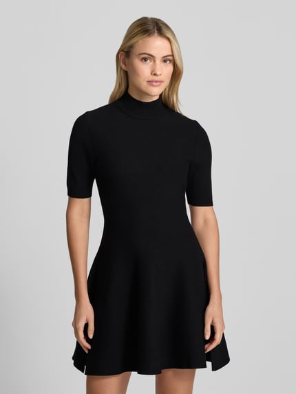 Frauenmodel trägt Minikleid aus Viskose-Mix mit Stehkragen von Apricot, A-Linie, kurzärmelig, schwarz, glatte Textur, Ganzkörperansicht von vorne.