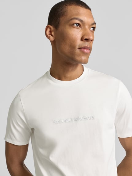 Männermodel trägt Regular Fit T-Shirt mit Logo-Detail von Emporio Armani aus reiner Baumwolle, Rundhalsausschnitt, Nahaufnahme Oberkörper.