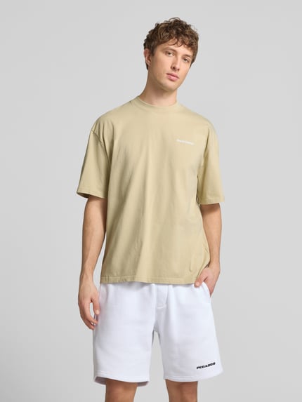 Männermodel trägt Oversized T-Shirt mit Logo-Stitching von Pegador in Beige, Reine Baumwolle, Oversized-Fit, Rundhalsausschnitt, Rückenlänge bei Größe M 73 cm, Herren T-Shirt, Ganzkörperansicht von vorne.