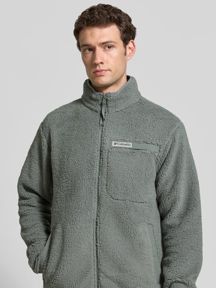 Männermodel trägt Regular Fit Fleecejacke mit Logo-Patch von Columbia in Grau, Fleece mit Stehkragen und Brusttasche, Nahaufnahme Oberkörper.