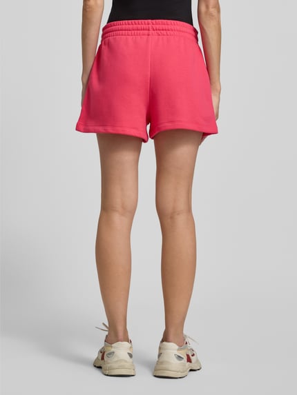Frauenmodel trägt Sweatshorts mit Logo und elastischem Bund von GAP in kräftigem Pink, Baumwoll-Mix, Regular-Fit, Ganzkörperansicht Rückansicht.