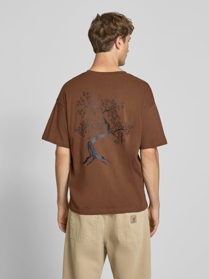 Männermodel trägt Relaxed Fit T-Shirt aus reiner Baumwolle Modell "DYLAN" von JACK & JONES in Braun mit Print-Detail, Ganzkörperansicht Rückansicht.