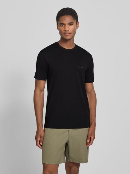 Męskimodel nosi Extra Slim Fit T-Shirt mit Rundhalsausschnitt von Armani Exchange, czarny kolor, logo, okrągły dekolt, długość tyłu w rozmiarze M: 70 cm, krój slim fit, Ganzkörperansicht von vorne.