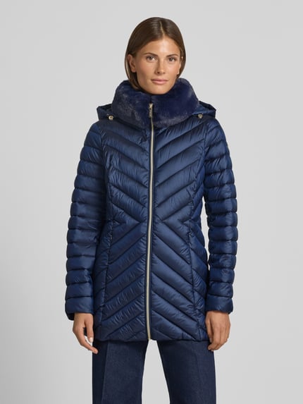 Frauenmodel trägt Parka mit Steppnähten und Kapuze von MICHAEL Michael Kors, navyblau, sichtbare Reißverschlüsse, seitliche Taschen, glatte glänzende Textur, gerader Schnitt, Ganzkörperansicht von vorne. Kontext: Steppnähte, Tunnelzugkapuze, Label-Detail, Rückenlänge 74 cm, Schulterbreite 40 cm, Brustweite 46 cm, Ärmellänge 62 cm.