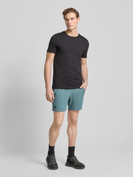 Męski model nosi Szorty z elastycznym pasem i logo od Under Armour, krój regular fit, detal z logo, jasnoniebieskie, szerokość w pasie 39 cm, długość wewnętrzna nogawki 17 cm, całkowity widok z przodu.