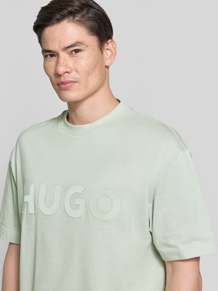 Männermodel trägt Relaxed Fit T-Shirt aus reiner Baumwolle Modell 'DINKEE' von HUGO, Optik: Unifarben, 3D Label-Print, Rundhals, Kurzarm, Materialverarbeitung: Jersey, Ganzkörperansicht von vorne.