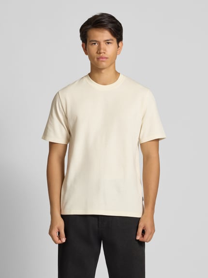 Męski model nosi t-shirt z elastycznej mieszanki materiałów z mieszanką bawełny, prosty krój, model 'AUSTIN' od Jack & Jones, stójka, długość tyłu w rozmiarze M: 70 cm, jasny kolor, gładka faktura, całkowity widok od przodu