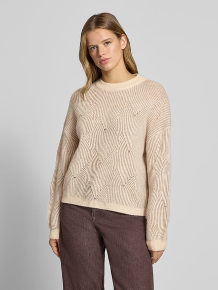 Frauenmodel trägt Pullover mit plastischer Strickstruktur von PIECES in Beige, geometrisches Allover-Muster, Rundhals, gerippte Abschlüsse, Ganzkörperansicht von vorne.