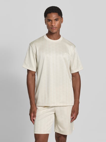 Männermodel trägt Regular Fit T-Shirt mit Allover-Muster von Lacoste in Creme mit feiner Struktur, Herren T-Shirt, Ganzkörperansicht von vorne.