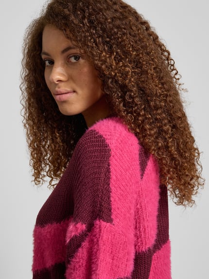 Frauenmodel trägt Loose Fit Strickpullover mit Rundhalsausschnitt Modell 'BLAIR' von Noisy May, pink-bordeaux Allover-Look, Nahaufnahme Oberkörper.