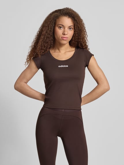 Modelka kobieca nosi Slim Fit Sport T-Shirt mit Label Print od adidas Sportswear, brązowy, krój slim fit, unikolor, stretch, nadrukowane logo, widok na cały przód, zdjęcie górnej części ciała.