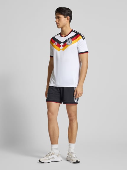 Männermodel trägt DFB Heimtrikot mit Label-Print von adidas Sportswear, weiß mit buntem Muster, Regular-Fit, Rundhalsausschnitt, gerippte Ärmelabschlüsse, Rückenlänge bei Größe M 73 cm, Ganzkörperansicht von vorne.