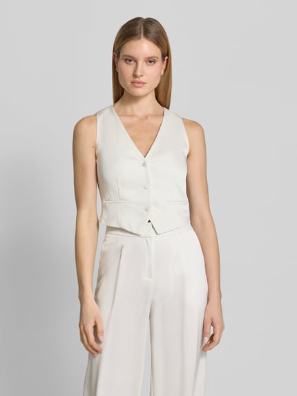 Kobiece modelka nosi Weste aus Satin mit V-Ausschnitt von Jake*s Cocktail, satyna, krój slim fit, dekolt w serek, listwa guzikowa, kieszenie z wypustkami, długość tyłu w rozmiarze 36: 40 cm, jasny kolor, gładka powierzchnia, Ganzkörperansicht von vorne.