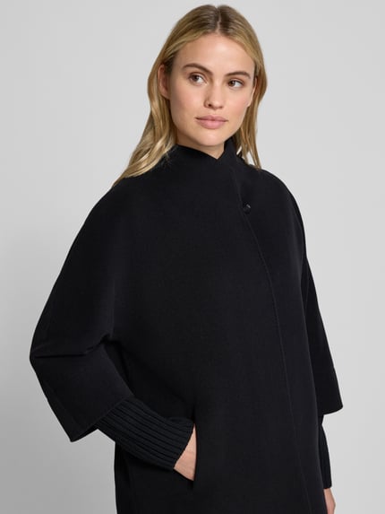 Frauenmodel trägt Jacke aus Lanawolle-Kaschmir-Mix mit herausnehmbarem Strickarm von ICONS Cinzia Rocca in Schwarz, glatte Textur, Stehkragen, Knopfverschluss, Eingrifftaschen, Regular Fit, Nahaufnahme Oberkörper.