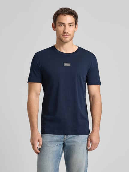 Männermodel trägt Regular Fit T-Shirt aus reiner Baumwolle von Tom Tailor Denim in Dunkelblau, unifarben, Label-Schriftzug, Ganzkörperansicht von vorne.