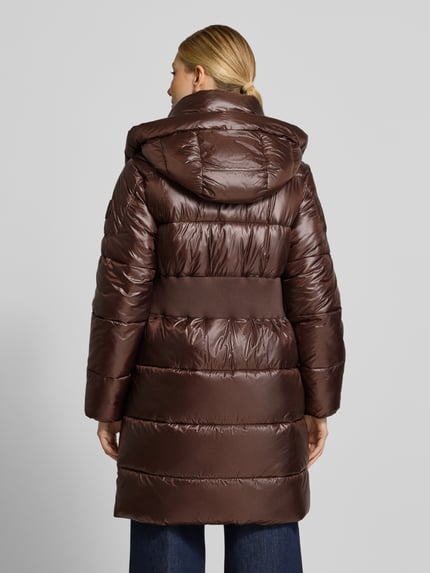 Frauenmodel trägt Steppmantel mit Kapuze von JOOP! in glänzendem Braun, Longline, mit metallischen Akzenten, Ganzkörperansicht Rückansicht.