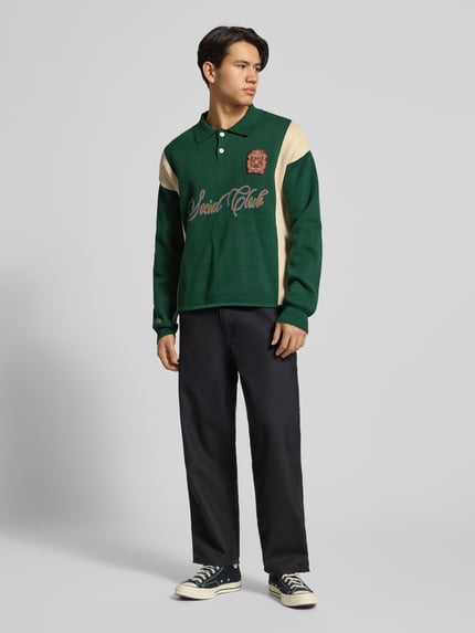 Männermodel trägt Strickpullover mit Polokragen und Label-Patch von PROHIBITED aus reiner Baumwolle, Relaxed-Fit, Ganzkörperansicht von vorne.