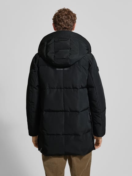 Männermodel trägt schwarzen Regular Fit Steppmantel mit Logo-Patch Modell 'Zeno' von khujo, gesteppte Struktur, Ganzkörperansicht Rückansicht.