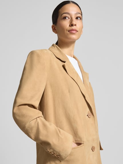 Vrouwenmodel draagt Ledermantel met Pattentaschen Modell 'Santara' van STAND STUDIO in lichtbruin geitenvelours, rechte fit, reverskraag, knoopsluiting, borstzak en klepzakken, detailopname bovenlichaam.
