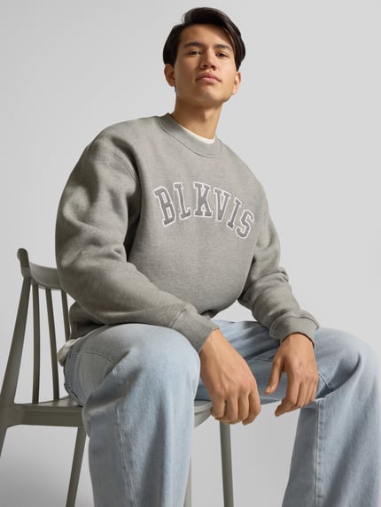 Männermodel trägt Sweatshirt mit Logo und Rundhalsausschnitt von BLKVIS, grau, reine Baumwolle, Relaxed Fit, Nahaufnahme Oberkörper.