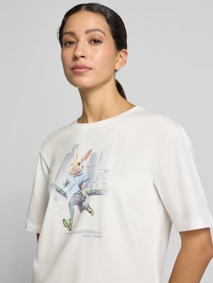 Vrouwenmodel draagt T-shirt met motiefprint van Marc Cain in wit, puur katoen, los model, ronde hals, ruglengte maat 36: 57 cm, close-up bovenlichaam