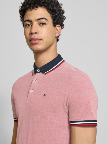 Mannelijk model draagt Slim Fit Poloshirt met viscose Model 'Paulos' van JACK & JONES in roze met polokraag, korte mouw, logostitching, mix van katoen en viscose, ruglengte maat M 72 cm. Nahaufnahme bovenlichaam.
