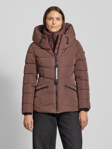 Kobiecy model nosi Steppjacke mit Kapuze od khujo, brązowa, regular fit, kaptur, stójka, zamek, kieszenie, widok całej sylwetki z przodu.