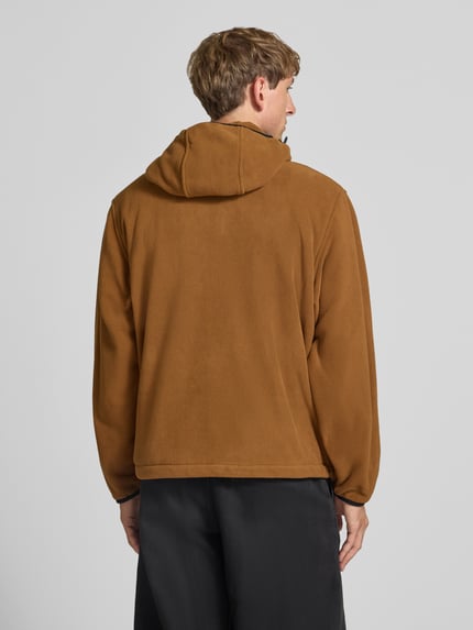 Männermodel trägt Fleecejacke mit Label-Patch Modell 'Blevin' von Carhartt Work In Progress in Braun, weiche Textur, Ganzkörperansicht Rückansicht. Herren Fleecejacke, Regular Fit, Kapuze, Zweiwege-Reißverschluss, seitliche Reißverschlusstaschen, Rückenlänge bei Größe M 68 cm, Ärmellänge 65 cm.
