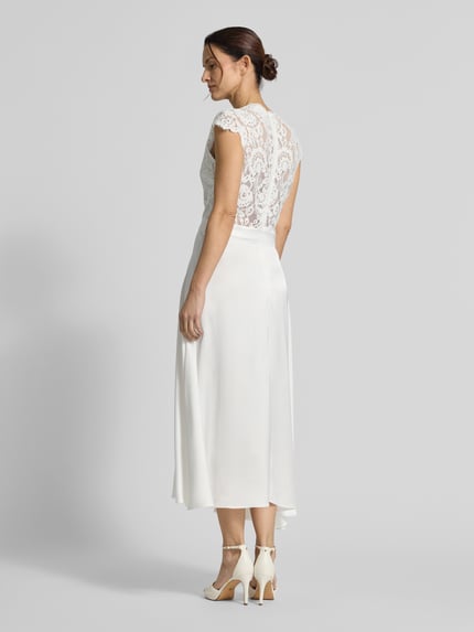 Modelka nosi Brautkleid in Midilänge Modell 'Lilia' von GUIDO MARIA KRETSCHMER WOMAN, biała koronka, gładki satynowy dół, midi, widok całej sylwetki z tyłu.