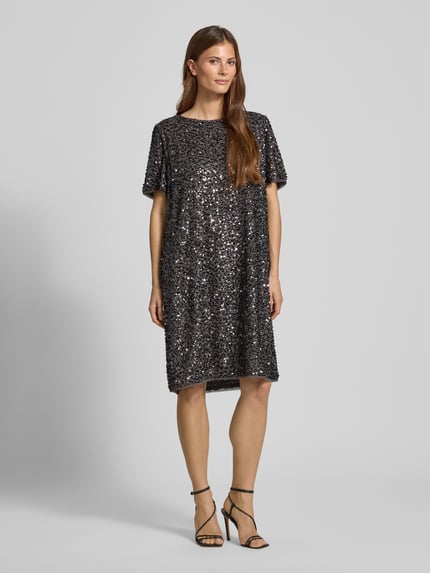 Vrouwenmodel draagt Knielanges Kleid mit Rundhalsausschnitt van Comma, los model, knielengte, met pailletten, ronde hals, met korte mouwen, ruglengte bij maat 36: 96 cm, borstwijdte 53 cm, mouwlengte 25 cm, geheel bedekt met glanzende textuur, donkere kleur, Ganzkörperansicht von vorne.