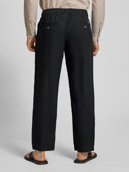 Mężczyzna nosi ciemne spodnie lniane z elastycznym pasem, model 'KARL LAWRENCE' od Jack & Jones, krój regular fit, szerokość w rozmiarze M: 40 cm, długość nogawki od wewnątrz w rozmiarze M: 75 cm, tkanina o wyraźnej lnianej fakturze, widok całej sylwetki z tyłu.