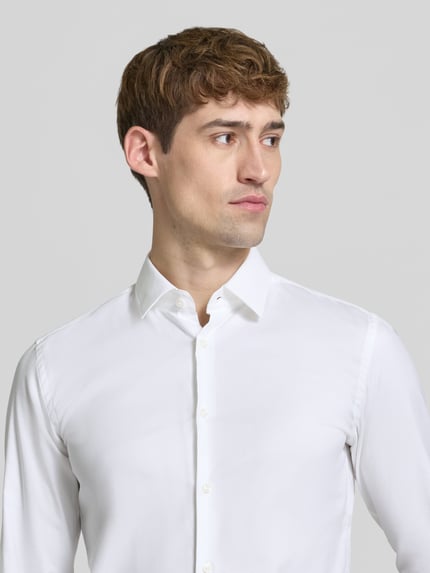 Männermodel trägt Slim Fit Businesshemd mit Kentkragen von BOSS in Weiß, strukturierte Webware, Nahaufnahme Oberkörper.