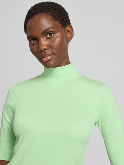 Kobiece model prezentuje Slim Fit T-Shirt aus Baumwoll-Mix mit Stehkragen od Marc Cain w kolorze jasnozielonym, mieszanka bawełny, krój slim fit, stójka, rękaw o dł. 1/2, Długość tyłu w rozmiarze 36: 54 cm, zbliżenie na górną część ciała