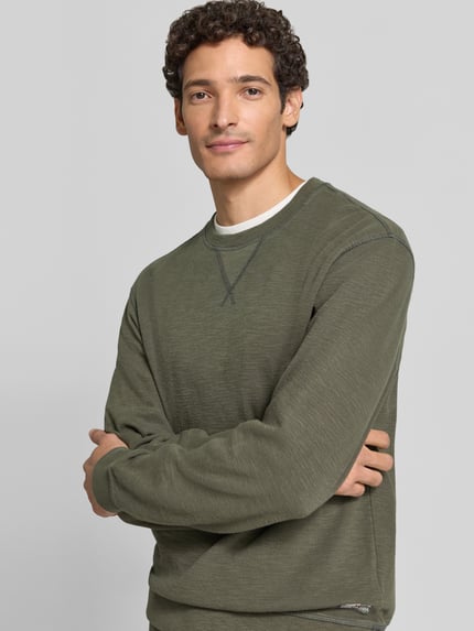 Męski model ma na sobie Regular Fit Sweatshirt aus Baumwoll-Mix od Scotch & Soda w odcieniu oliwkowej zieleni, tekstura melanżowa, okrągły dekolt, elastyczne wykończenia, długość tyłu w rozmiarze M: 61 cm, długość rękawa w rozmiarze M: 70 cm, zdjęcie górnej części ciała z przodu.