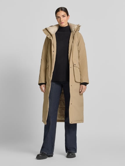Frauenmodel trägt Regular Fit Parka mit Kapuze Modell 'Melody' von Didriksons in Beige mit aufgesetzten Taschen, elastischen Ärmelabschlüssen, Ganzkörperansicht von vorne. Rückenlänge 111 cm, Schulterbreite 42 cm, Brustweite 53 cm, Ärmellänge 65 cm.