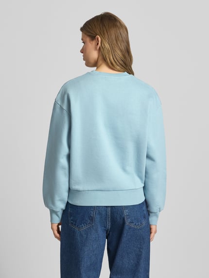 Vrouwenmodel draagt lichtblauw dames sweatshirt van puur katoen, loose fit, model 'CASEY' van Carhartt Work In Progress, gestikt logo. Ganzlichaamsaanzicht achterkant.