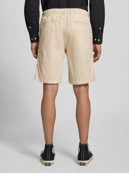 Męski model nosi szorty z tunel w kolorze beżowym, mieszanka bawełny i lnu, krój regular fit, Jack & Jones Shorts mit Tunnelzug Modell 'JAIDEN', szerokość w rozmiarze M 43 cm, długość wewnętrzna nogawki w rozmiarze M 23 cm, zdjęcie całej sylwetki z tyłu